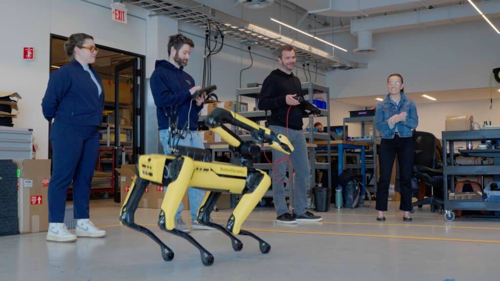 In a lab, four Boston Dynamics employees gather around a dancing quadruped robot to program and test performances
